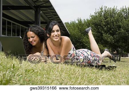 Teenage girl using a laptop with her friend lying beside her in a park View Large Photo Image Stock Photograph - Teenage girl using a laptop with her friend lying beside her in a park. Fotosearch