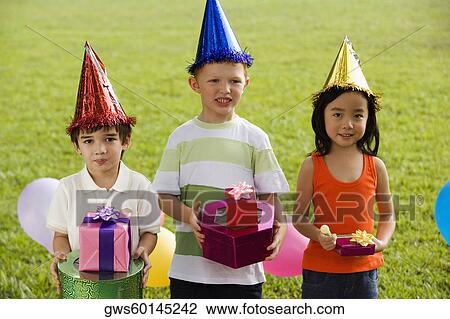 Three children standing together and holding gifts View Large Photo Image Stock Image - Three children standing together and holding gifts. Fotosearch