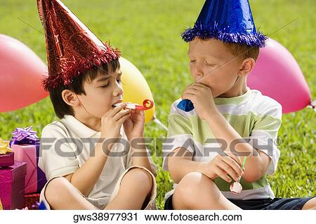 Stock Image - Two boys sitting together and blowing party horns. Fotosearch