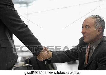 Two businessmen shaking hands at an airport View Large Photo Image Stock Photograph - Two businessmen shaking hands at an airport. Fotosearch