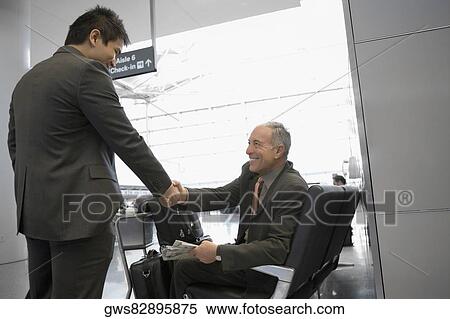 Stock Photography - Two businessmen shaking hands at an airport. Fotosearch