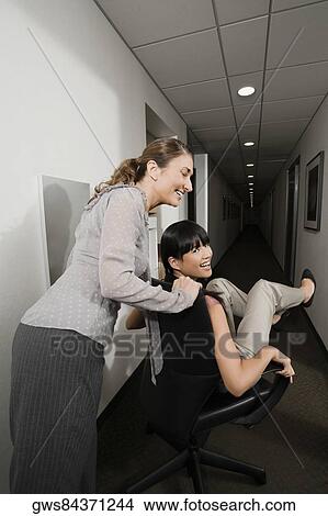 Two businesswomen playing in an office corridor View Large Photo Image Picture - Two businesswomen playing in an office corridor. Fotosearch