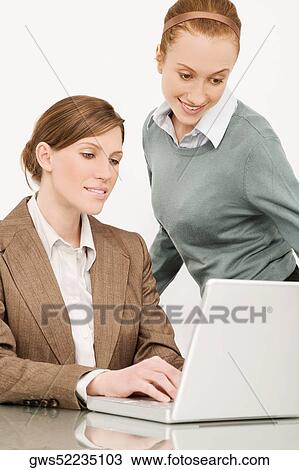 Stock Image - Two businesswomen working on a laptop and smiling. Fotosearch