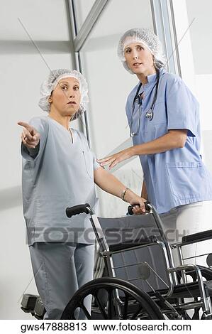 Stock Image - Two female surgeons standing near a wheelchair. Fotosearch
