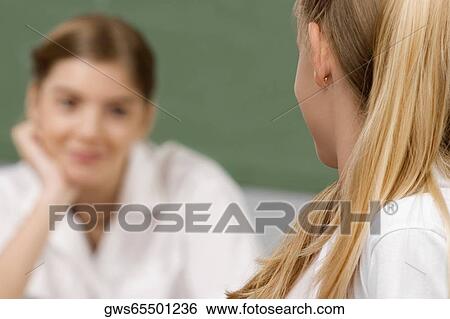Two schoolgirls looking at each other in a classroom View Large Photo Image Stock Photograph - Two schoolgirls looking at each other in a classroom. Fotosearch