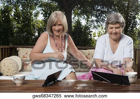 Stock Photography - Two women sitting on a couch and playing mahjong. Fotosearch