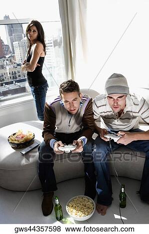 Two young men playing video game with a young woman standing behind them View Large Photo Image Stock Photo - Two young men playing video game with a young woman standing behind them. Fotosearch