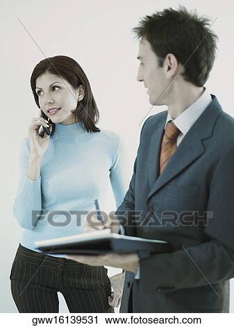 Stock Image - Businessman holding a personal organizer and looking at a businesswoman using a mobile phone. Fotosearch