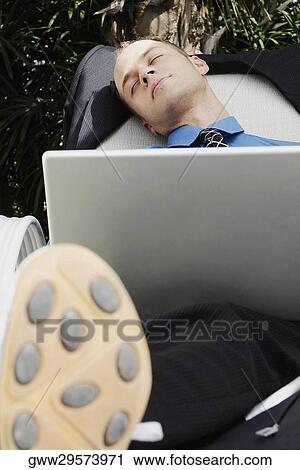 Businessman sleeping on a lounge chair with a laptop on his lap View Large Photo Image Stock Image - Businessman sleeping on a lounge chair with a laptop on his lap. Fotosearch
