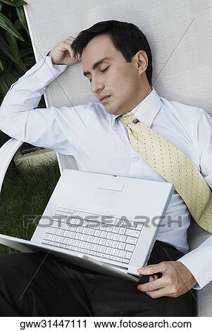 Businessman sleeping on a lounge chair with a laptop on his lap View Large Photo Image Stock Image - Businessman sleeping on a lounge chair with a laptop on his lap. Fotosearch