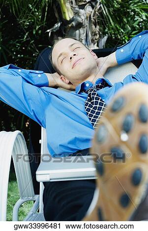 Businessman sleeping on a lounge chair with a laptop on his lap View Large Photo Image Stock Image - Businessman sleeping on a lounge chair with a laptop on his lap. Fotosearch