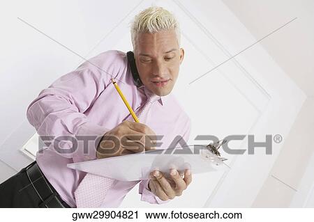 Businessman talking on a mobile phone and writing on a clipboard View Large Photo Image Stock Image - Businessman talking on a mobile phone and writing on a clipboard. Fotosearch