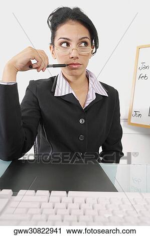 Stock Image - Businesswoman holding a pen and thinking. Fotosearch