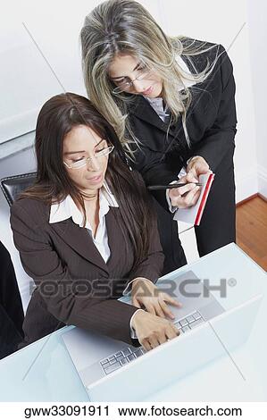 Businesswoman using a laptop with another businesswoman writing on a notepad View Large Photo Image Stock Image - Businesswoman using a laptop with another businesswoman writing on a notepad. Fotosearch