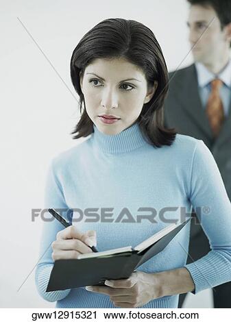 Stock Image - Businesswoman writing on a personal organizer with a businessman standing behind her. Fotosearch