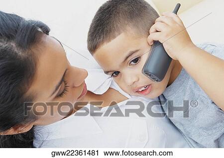 Stock Image - Close-up of a boy talking on a mobile phone with his mother beside him. Fotosearch