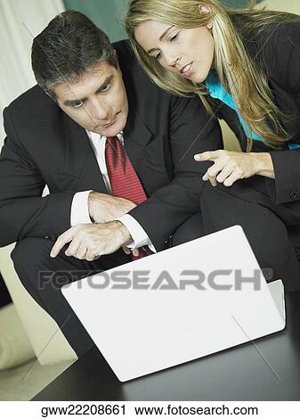 Close-up of a businessman and a businesswoman sitting in front of a laptop View Large Photo Image Stock Image - Close-up of a businessman and a businesswoman sitting in front of a laptop. Fotosearch