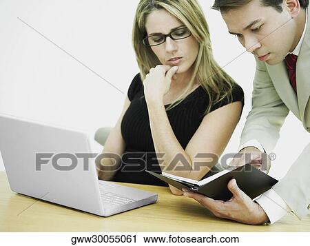 Stock Image - Close-up of a businessman and a businesswoman in front of a laptop and looking at a diary. Fotosearch