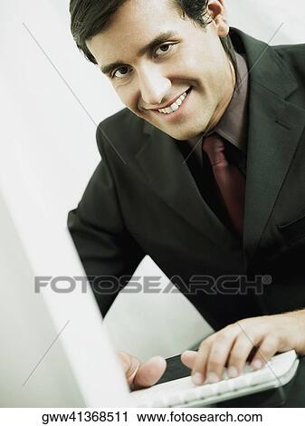 Stock Image - Close-up of a businessman smiling and working on a laptop. Fotosearch