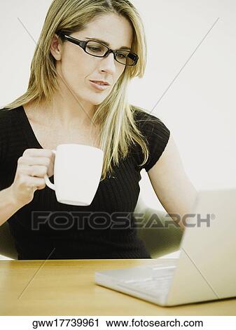 Close-up of a businesswoman holding a cup and sitting in front of a laptop View Large Photo Image Stock Image - Close-up of a businesswoman holding a cup and sitting in front of a laptop. Fotosearch