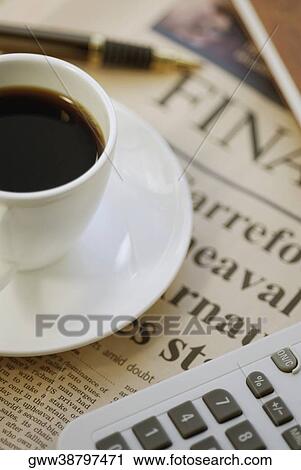 Stock Image - Close-up of a cup of tea with a calculator on a financial newspaper. Fotosearch