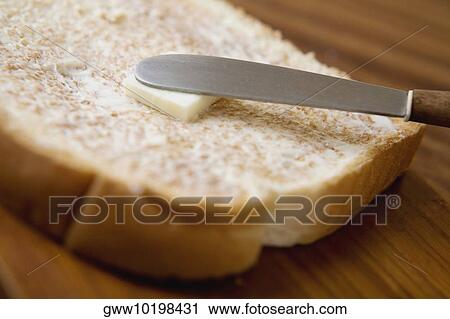 Stock Image - Close-up of a knife spreading peanut butter on a slice of bread. Fotosearch
