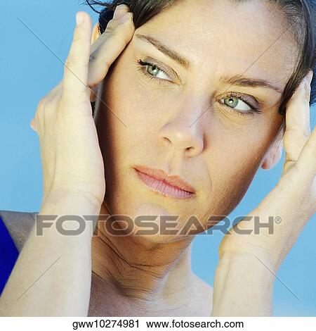 Stock Image - Close-up of a mature woman holding her temple. Fotosearch