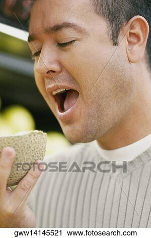 Close-up of a mid adult man eating a cantaloupe View Large Photo Image Stock Image - Close-up of a mid adult man eating a cantaloupe. Fotosearch