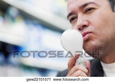Stock Image - Close-up of a mid adult man holding a light bulb and thinking. Fotosearch
