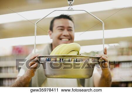 Close-up of a mid adult man holding a weighing scale and smiling View Large Photo Image Stock Image - Close-up of a mid adult man holding a weighing scale and smiling. Fotosearch