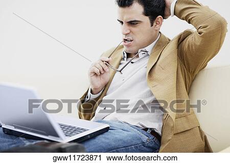 Stock Image - Close-up of a mid adult man sitting with a laptop and thinking. Fotosearch
