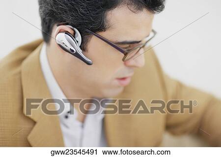 Stock Image - Close-up of a mid adult man wearing a hands free device. Fotosearch