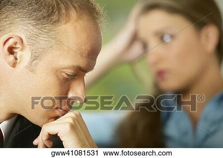 Close-up of a mid adult man with his hand on his chin and a young man in the background View Large Photo Image Stock Image - Close-up of a mid adult man with his hand on his chin and a young man in the background. Fotosearch