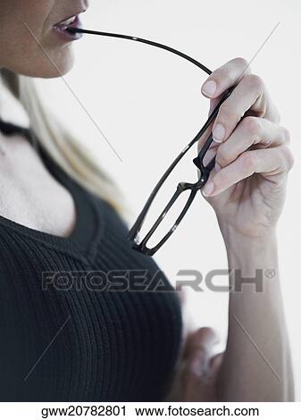 Stock Image - Close-up of a mid adult woman biting a pair of eyeglasses. Fotosearch