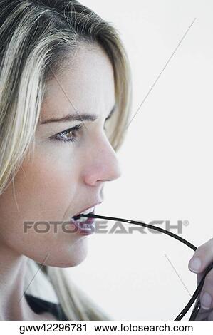 Stock Image - Close-up of a mid adult woman biting a pair of eyeglasses. Fotosearch