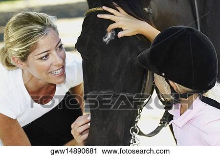 Stock Image - Close-up of a mid adult woman with her daughter touching a horse. Fotosearch