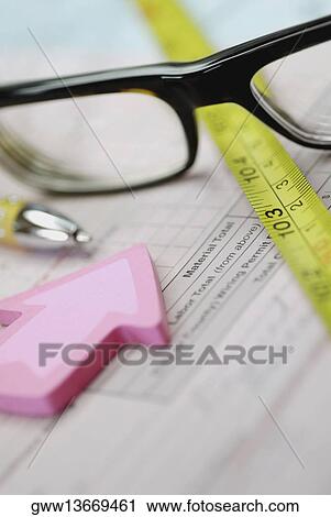 Stock Image - Close-up of a pair of eyeglasses with a tape measure and a pen on a document. Fotosearch