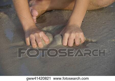 Stock Image - Close-up of a person playing with sand on the beach. Fotosearch