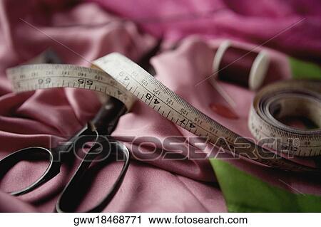 Stock Image - Close-up of a tape measure with a pair of scissors on fabric. Fotosearch