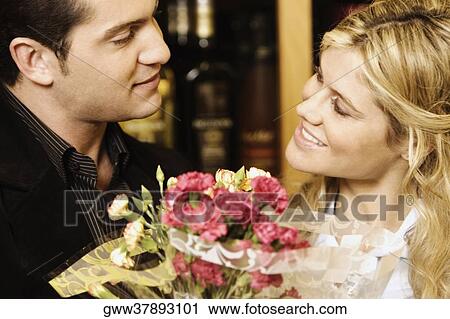 Stock Image - Close-up of a young couple holding a bouquet of flowers in a liquor store. Fotosearch