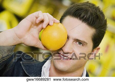 Close-up of a young man covering his eye with an orange View Large Photo Image Stock Image - Close-up of a young man covering his eye with an orange. Fotosearch