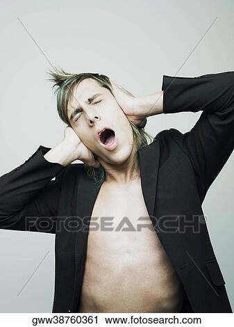 Stock Image - Close-up of a young man covering his ears with his hands and screaming. Fotosearch