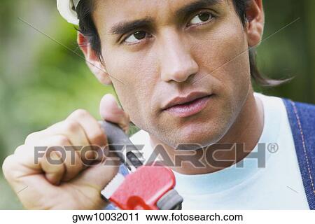 Stock Image - Close-up of a young man holding an adjustable wrench. Fotosearch