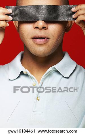 Stock Image - Close-up of a young man holding duct tape in front of his eyes. Fotosearch