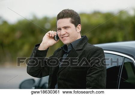 Close-up of a young man leaning against a car and talking on a mobile phone View Large Photo Image Stock Image - Close-up of a young man leaning against a car and talking on a mobile phone. Fotosearch