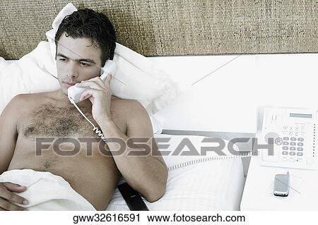 Close-up of a young man lying on the bed and talking on the telephone View Large Photo Image Stock Image - Close-up of a young man lying on the bed and talking on the telephone. Fotosearch