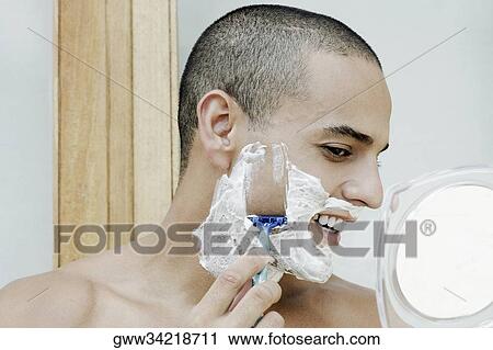 Stock Image - Close-up of a young man shaving in the bathroom. Fotosearch