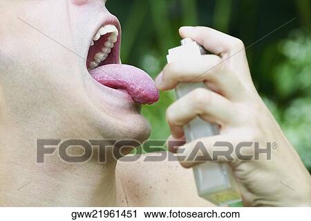 Stock Image - Close-up of a young man spraying perfume on his tongue. Fotosearch