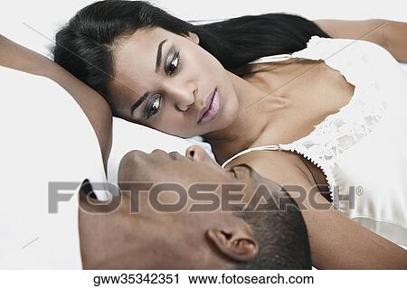 Stock Image - Close-up of a young woman and a mid adult man lying on the bed. Fotosearch