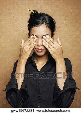 Stock Image - Close-up of a young woman covering her eyes with her hands. Fotosearch